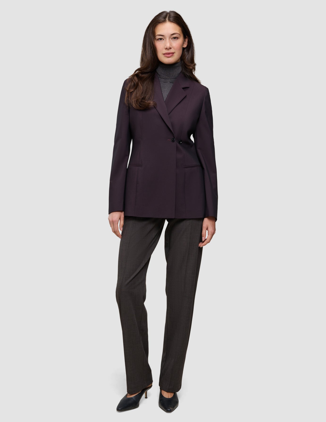 En kvinne som har på seg en Women’s Avira Blazer Burgundy Berry over en grå turtleneck og mørke bukser med svarte høyhælte sko.